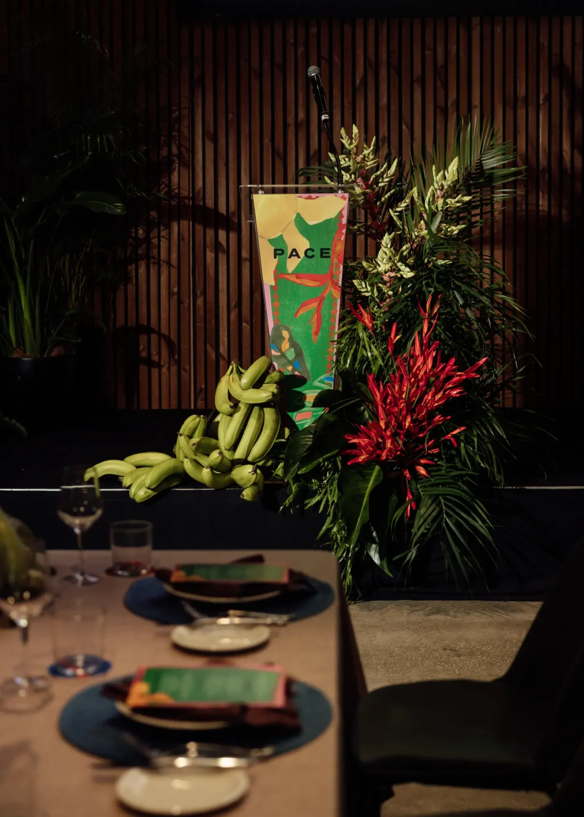 Lectern with a branded banner, green bananas and tropical florals at a corporate event at Half Acre