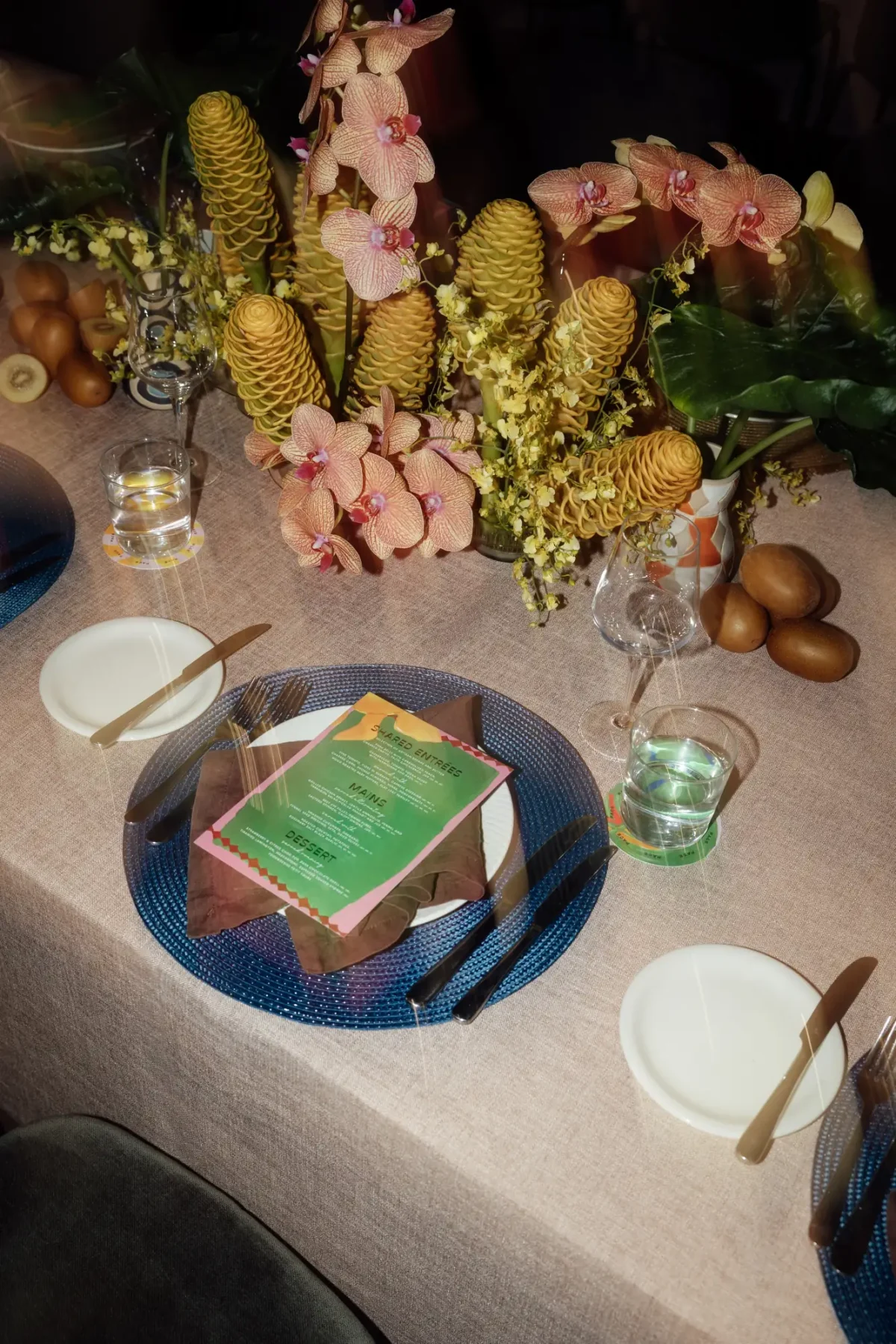 Place setting with a printed menu, blue woven placemat and orchid and banksia centrepiece
