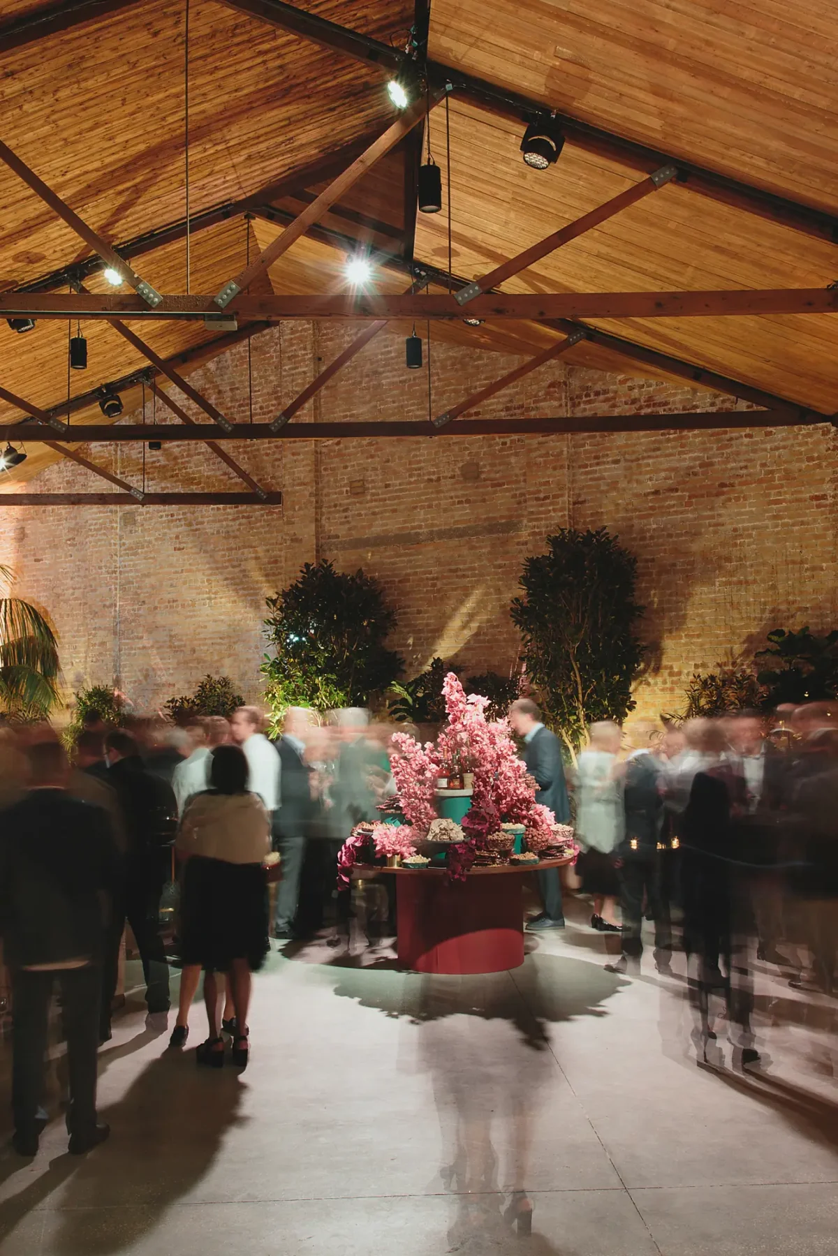Guests mingling around a pink floral centrepiece beneath the timber trusses of The Mill at Half Acre