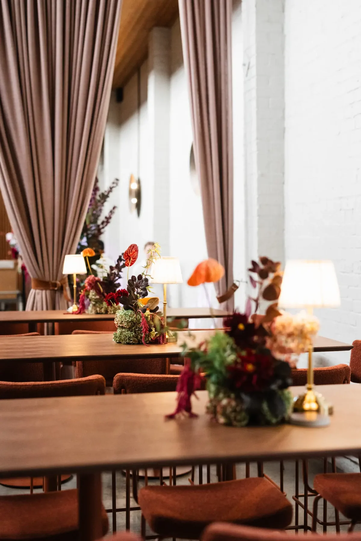 Timber tables set with lamps and bright florals beside linen drapes at Half Acre