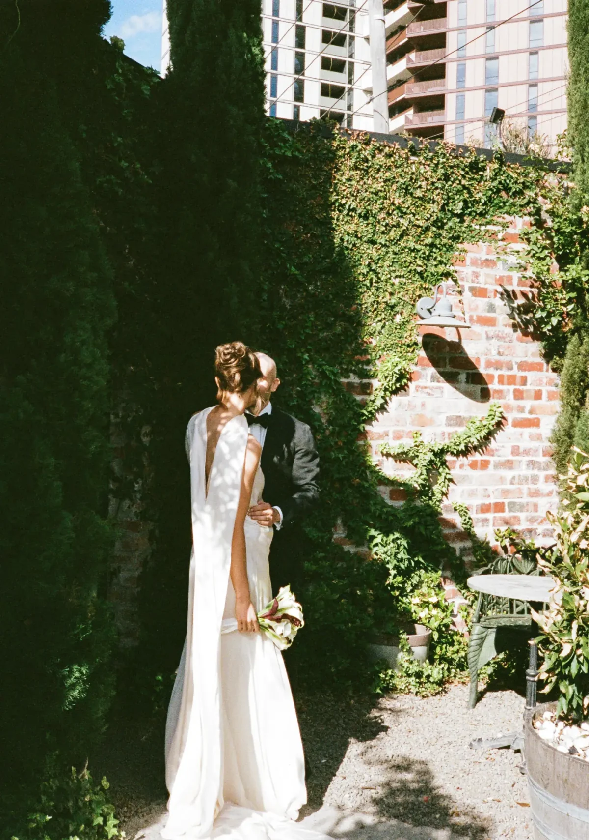 Bride and groom embracing beside the ivy-covered brick wall in The Courtyard at Half Acre