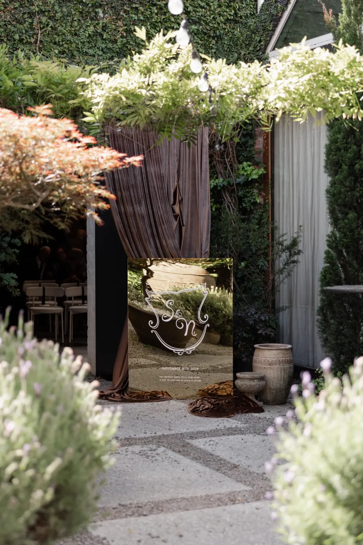 Mirrored wedding welcome sign framed by wisteria and lavender in The Courtyard at Half Acre