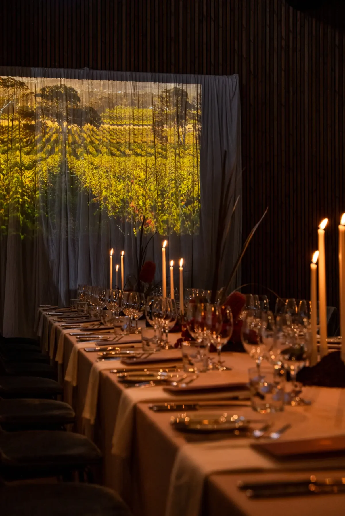 Candlelit long dining table in The Mill at Half Acre with a vineyard projection on sheer drapes