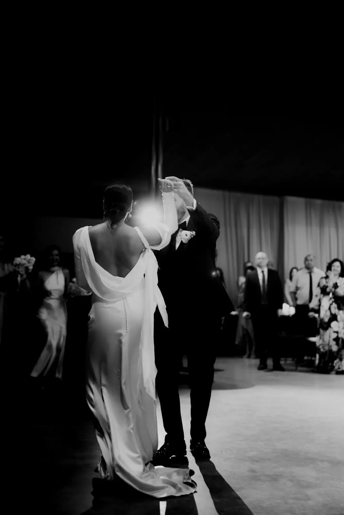 Black and white photo of a couple's first dance at Half Acre as guests look on