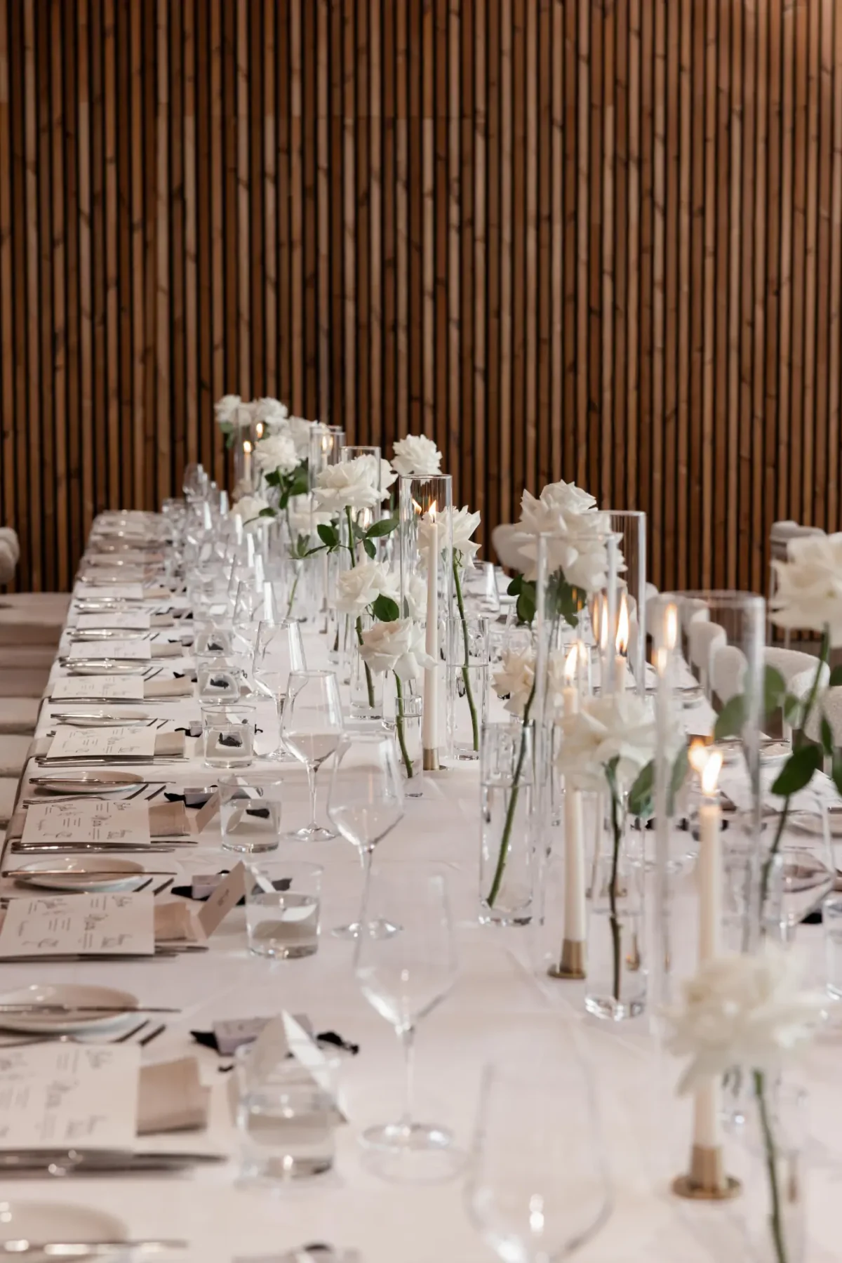 Wedding table set with white roses, candles and glassware against the timber wall of The Mill