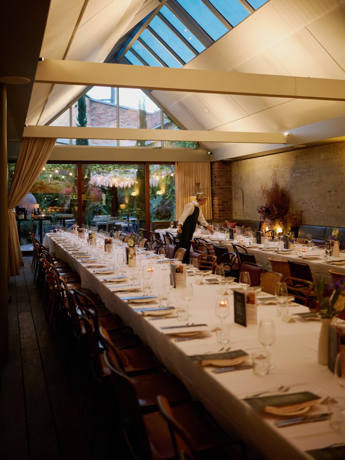 Long dinner tables set beneath the glass roof of The Atrium at Half Acre