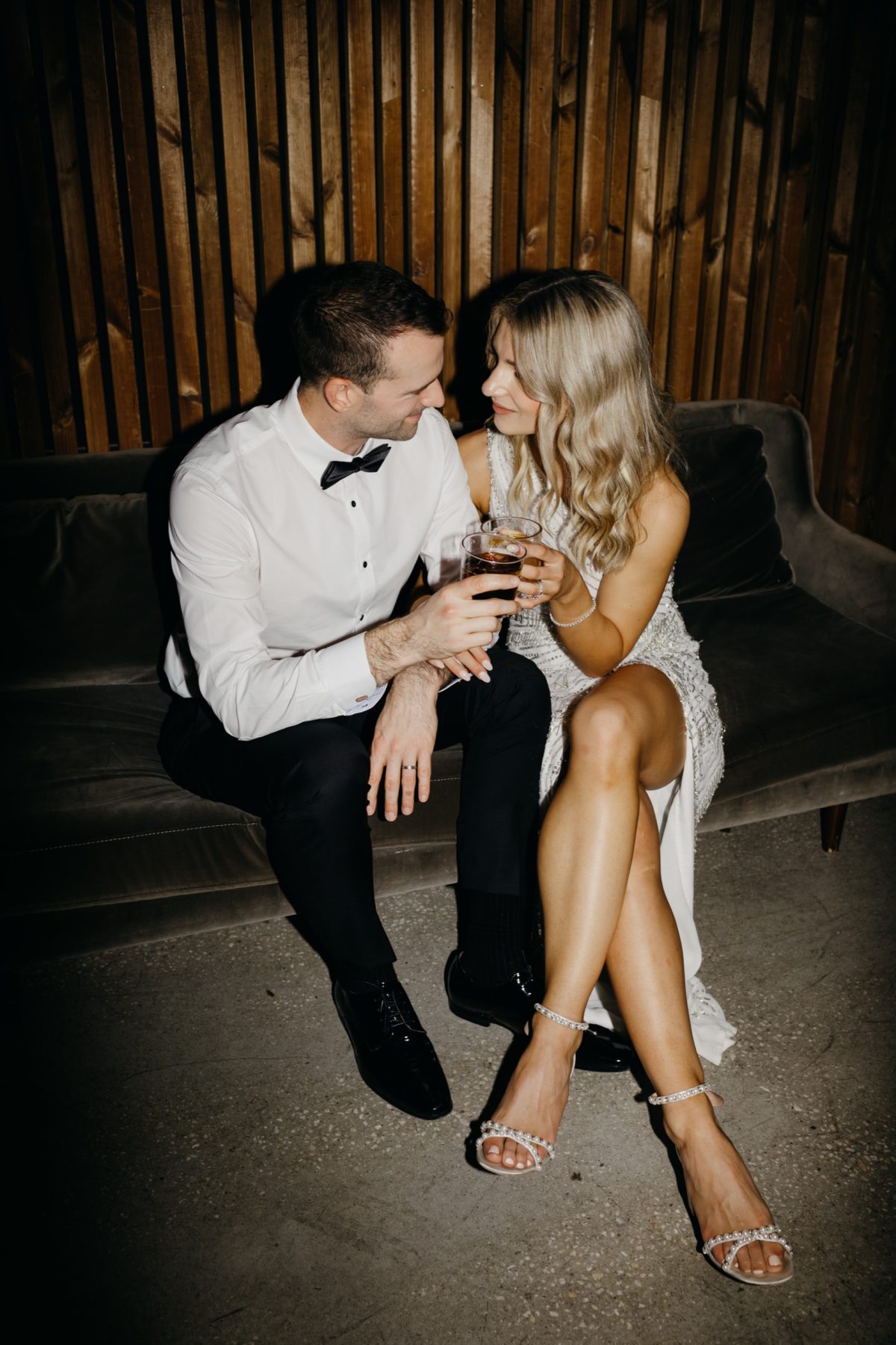 Bride and groom sharing a drink on a lounge against the timber wall at Half Acre